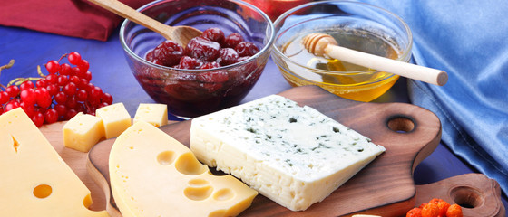 Cheese platter: variety of cheeses on wooden plate with fruits. Different types of cheese and honey. Hard cheese and berries on a classic blue background. Top view