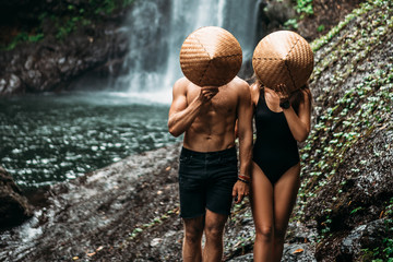 The couple travels the world. Vacation in Asia. A couple in love on a waterfall. Man and woman in conical hats at a waterfall. Beautiful couple traveling in Bali. Travelers at the waterfall. 