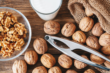 Close up top view of cracked walnuts with nutcracker and a glass of milk on a wooden table. Healthy life concept
