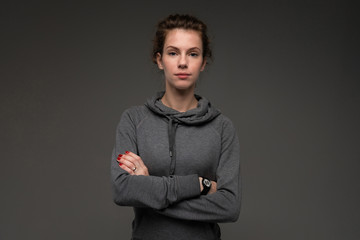 attractive caucasian girl in a gray sweatshirt with arms crossed on a black background