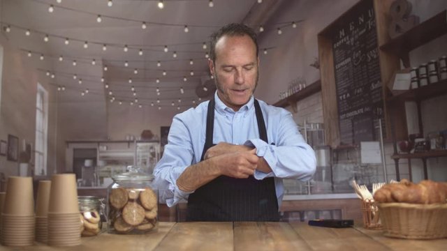 Happy handsome mature barista is getting ready for the work in a coffee shop. Looking at camera and smiling. Businessman.