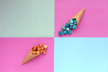 Popcorn spill out from waffle ice cream cone on pastel colorful background. Blue and caramel...