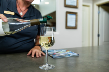 female bartender woman pouring white wine from transparent bottle to a wineglass, hand selective focus, with a magazine on bar counter, copy space