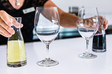 female bartender hands on small mini decanters filled with red and white wines. next to two wine empty glasses on bright white tasting room bar counter
