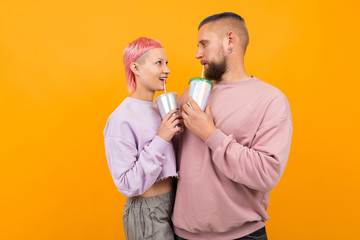 Unusual pretty woman with short pink hair and tattoo drinks coffee and having fun with her boyfriend isolated on orange background