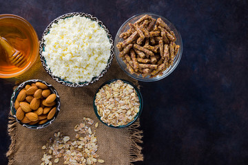 Healthy diet breakfast on burlap. Ingredients for a healthy breakfast - oatmeal, granola, honey, almonds, cottage cheese. Homemade granola on a dark background. Rustic style