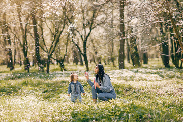 Naklejka na ściany i meble Beautiful mother with daughter. Family in a spring park. Woman in a blue jacket