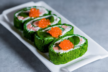 Spinach biscuit roll with cottage cheese, salted salmon and red caviar on a white rectangular plate on a gray table.