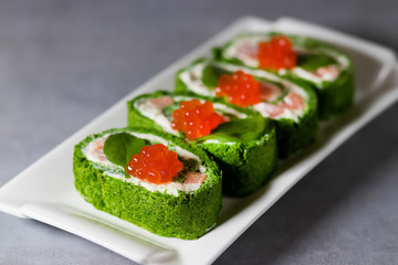 Spinach biscuit roll with cottage cheese, salted salmon and red caviar on a white rectangular plate on a gray table.