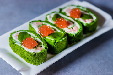 Spinach biscuit roll with cottage cheese, salted salmon and red caviar on a white rectangular plate on a gray table.