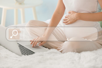 Beautiful pregnant woman with laptop sitting on bed
