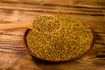 Ceramic plate and spoon with fenugreek seeds on wooden table