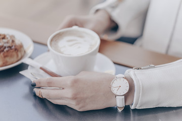 White watch on woman hand. Holding coffee cup.