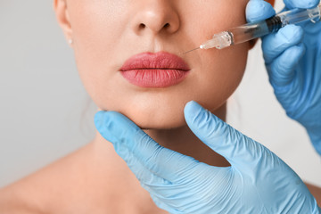 Young woman receiving filler injection against grey background, closeup