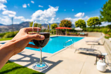 red wine glass on hand selective focus close up against winery restaurant patio with swimming pool background, Okanagan Valley British Columbia Canada
