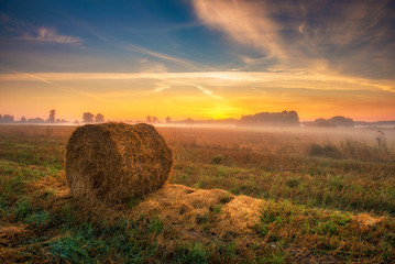 Beautiful summer sunrise over fields with hay bales