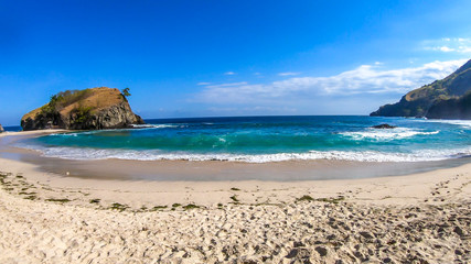A panoramic view on idyllic Koka Beach. Hidden gem of Flores, Indonesia. Beach is gently washed by waves. Steep hills going straight into the sea. Soft clouds on the sky. Serenity and calmness