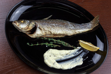 baked sea bass with sauce and lemon in a plate	