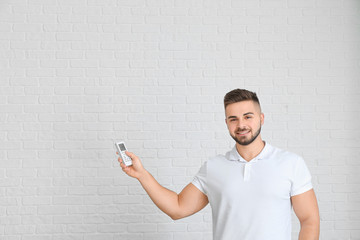 Young man with air conditioner remote control on light background
