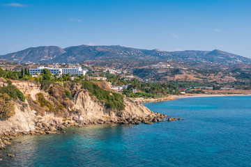 Fototapeta na wymiar Cyprus landscape. White buildings on stone hill near sea bay with clear transparent water on background of mountains.