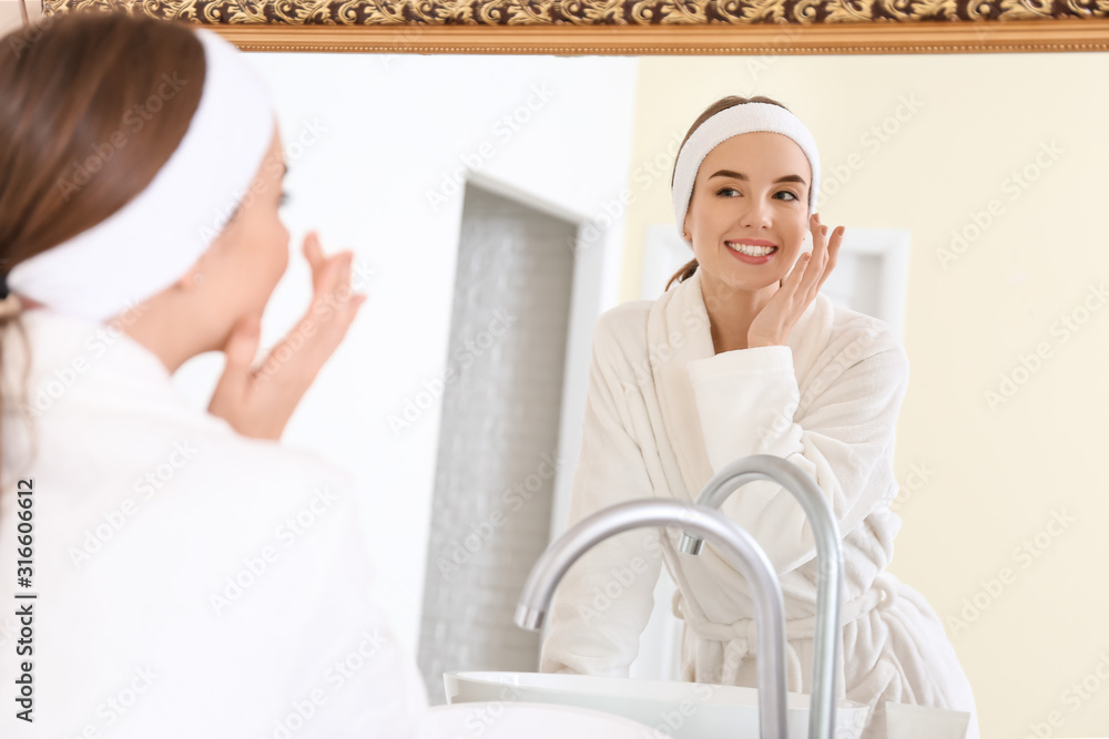 Sticker beautiful young woman applying cream on her face near mirror in bathroom