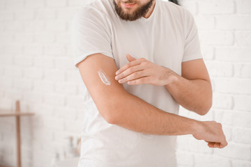 Handsome young man applying cream on his arm in bathroom