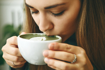 Close-up face or portrait of a girl who drinks healthy and delicious green matcha latte tea
