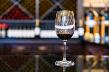 A glass of red wine on black marble countertop selective focus close up view against wine bottles on storage Racks, tasting room blurred background