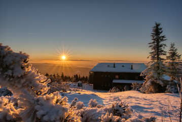 Golden sunlight over a idyllic white winter landscape with a little wooden hut in background ,...