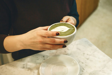 Barista holds a fragrant and healthy matcha latte tea in her hands.