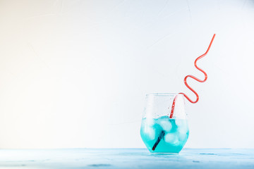 blue cocktail in a glass with ice with a red straw on a white concrete background on a blue table