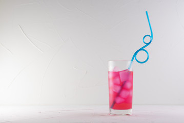 pink cocktail in a glass with ice with a blue straw on a white concrete background on a blue table