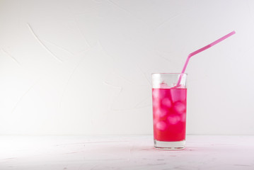 pink cocktail in a glass with ice with a pink straw on a white concrete background on a blue table