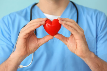 Male cardiologist with red heart on color background, closeup