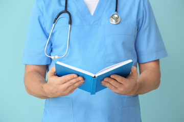 Male cardiologist with book on color background