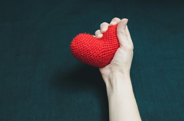 Female hand grips a red heart tightly