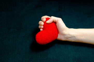 Female hand grips a red heart tightly