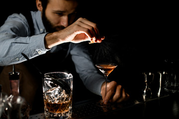 Male bartender spraying on a golden alcoholic drink in a martini glass with orage zest juice