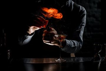 Male bartender spraying on a lighter with orage zest juice to golden alcoholic drink in a martini glass