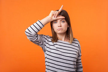 Portrait of upset disappointed young woman with brown hair in long sleeve striped shirt standing,...