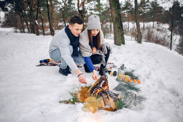 Couple in a winter forest. Beautiful girl in a blue sweater. Boy and girl sitting near bonfire