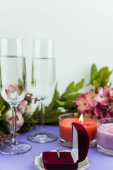 Marriage proposal and love concept for Valentine`s day, box with wedding or engagement ring with brilliant. Glass of champagne, romantic dinner, peony flowers and candles on trendy purple background