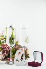 Marriage proposal and love concept for Valentine`s day, box with wedding or engagement ring with brilliant. Glass of champagne, romantic dinner, peony flowers and candles on white background