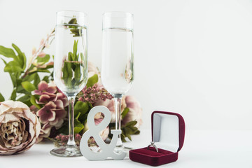 Marriage proposal and love concept for Valentine`s day, box with wedding or engagement ring with brilliant. Glass of champagne, romantic dinner, peony flowers and candles on white background