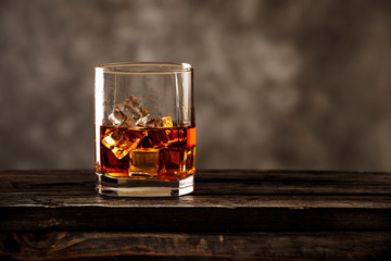 Whiskey with ice or brandy in a glass on a rustic table and gray background. Whiskey with ice in a glass. Whiskey or cognac in a glass. Selective focus.