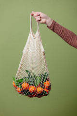 Woman hand holds mandarins in a string bag