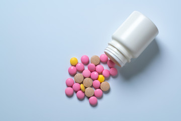 Multi-colored medical pills spilled out of a white jar on a white background