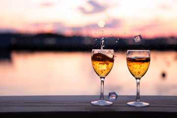 Two Glasses of white wine and drops of ice cubes against red sunset in yachting port. Beautiful summer evening sea view. Vacation for couple. Romantic evening
