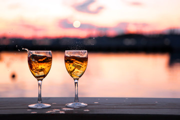 Two Glasses of white wine and drops of ice cubes against red sunset in yachting port. Beautiful summer evening sea view. Vacation for couple. Romantic evening