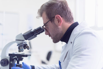 Young male scientist looking through a microscope in a laboratory doing research, microbiological analysis, medicine.